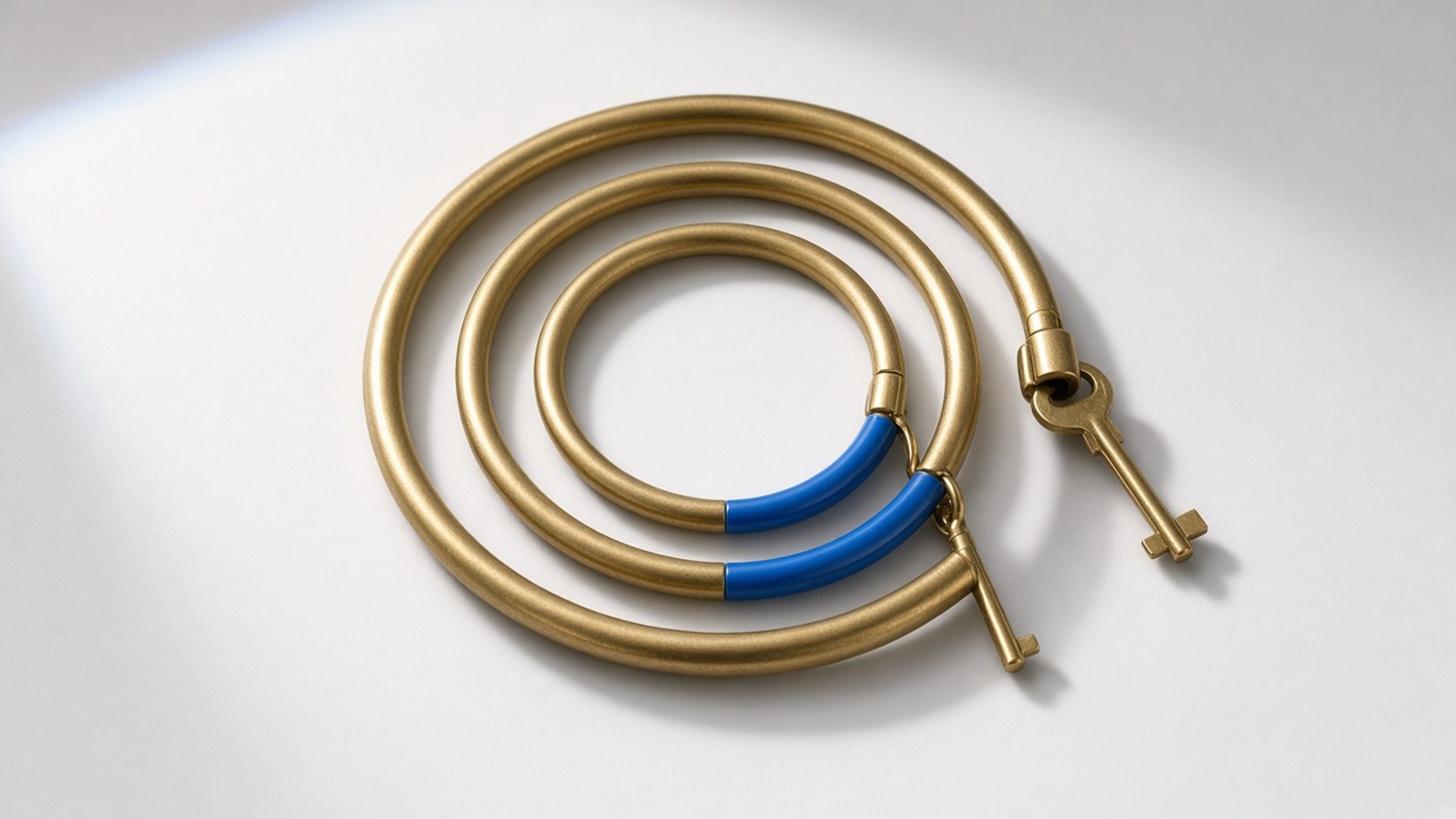Three nested brass keyrings with a blue accent on the inner ring, studio sweep
