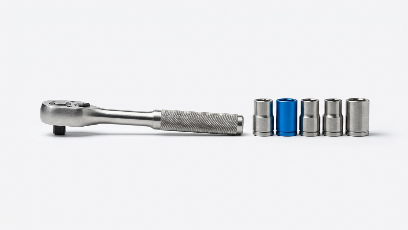 A steel ratchet wrench beside five interchangeable sockets, one socket enameled vivid blue, on a paper-white studio sweep